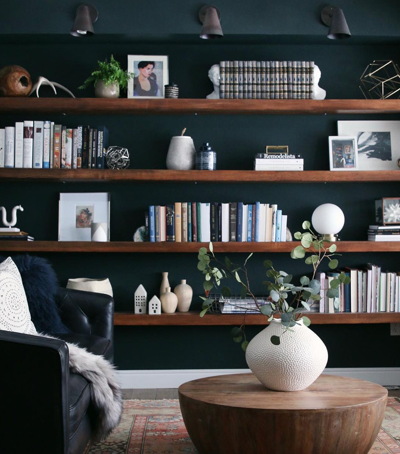 How To Organize a Bookshelf in Dark green room with wood book shelves, wood coffee table, vase with flowers, black leather chair, books, art, lighting.