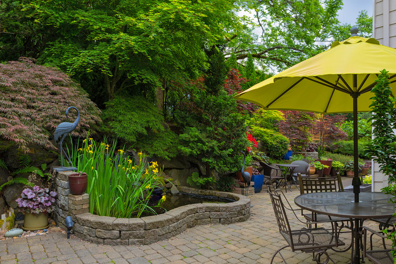 Home backyard hardscape and lush plants landscaping with garden furniture on paver brick patio.