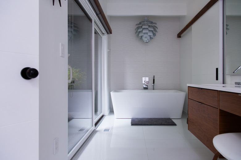 white freestanding tub, decorative hanging pendant above the bath, wood vanity, glass shower door