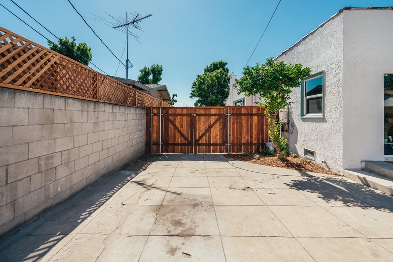 A concrete-wood-trellis fence and a Spanish style white house with terra-cotta tile roofing