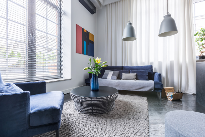 Gray living room with blue upholstered furniture, white mini blinds and curtains, gray pendant lamps.