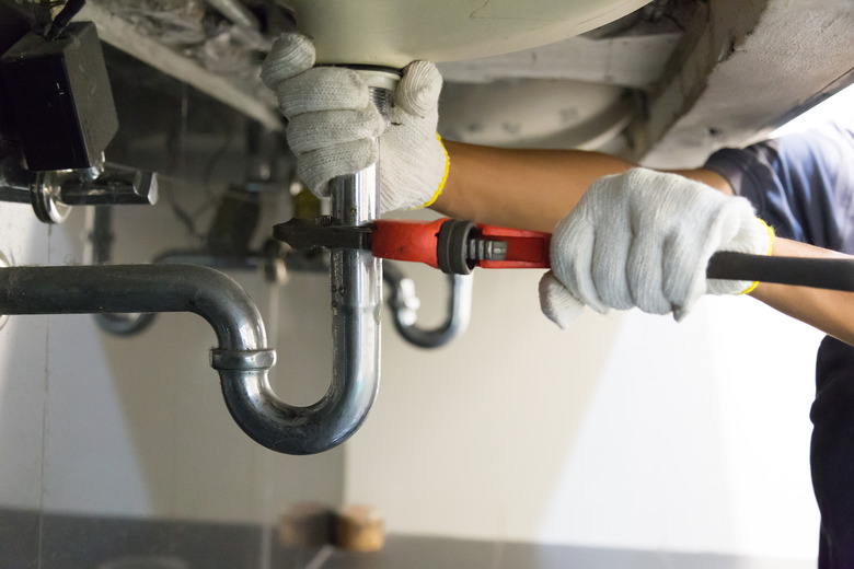 Plumber fixing white sink pipe with adjustable wrench.