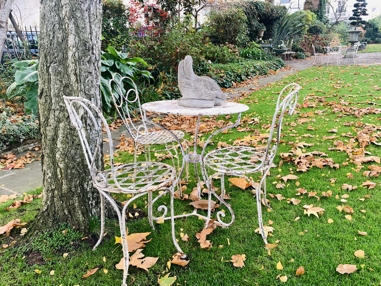 Iron chairs and table in garden with autumn leaves.