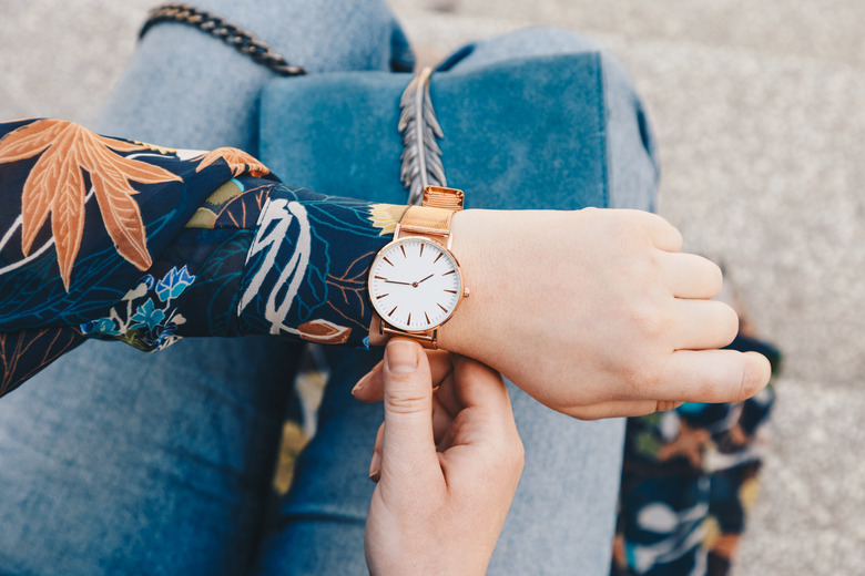 close up, young fashion blogger wearing a floral jacker, and a white and golden analog wrist watch. checking the time, holding a beautiful suede leather purse.