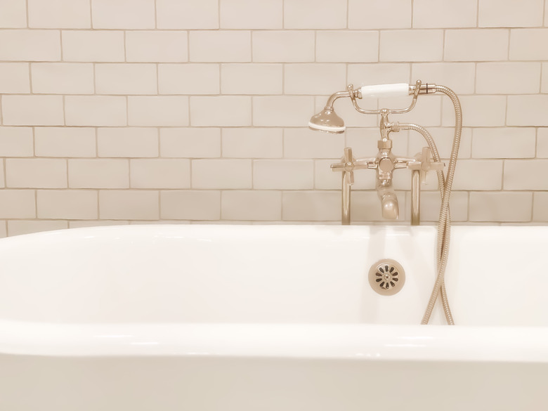 Old-fashioned polished nickel cross handle bathtub faucet & handheld sprayer with white enameled antique cast iron claw foot tub.