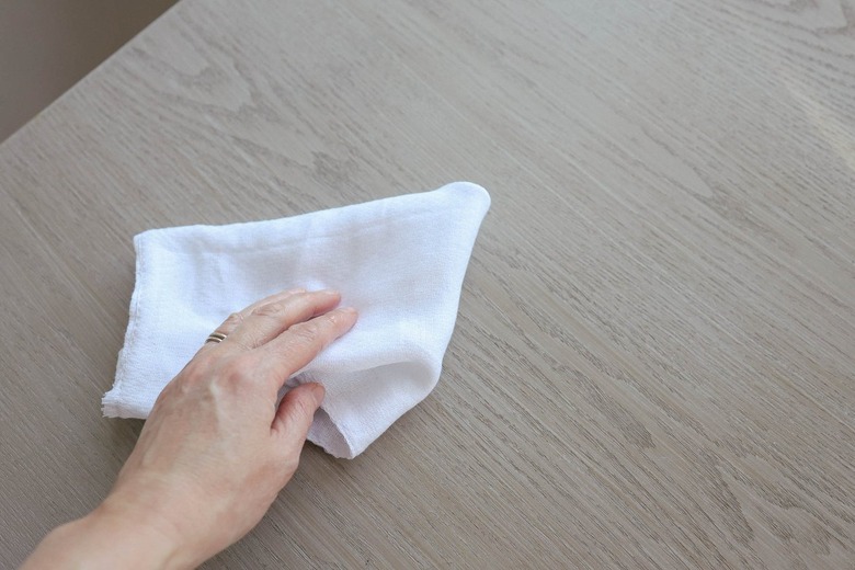 Person using a drop cloth to clean a wood tabletop with household surface cleaner or degreaser