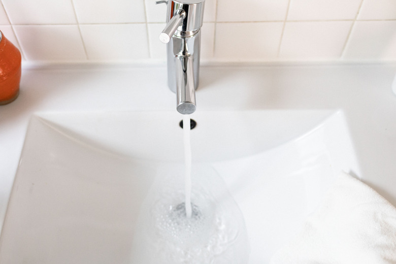 white ceramic sink, silver faucet with water running, white square tiles on the wall