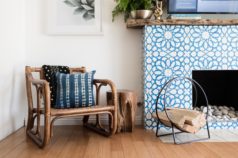 Boho chair, with a Shibori pillow, black-white patterned blanket, and a Moroccan star tile, wood mantel fireplace.