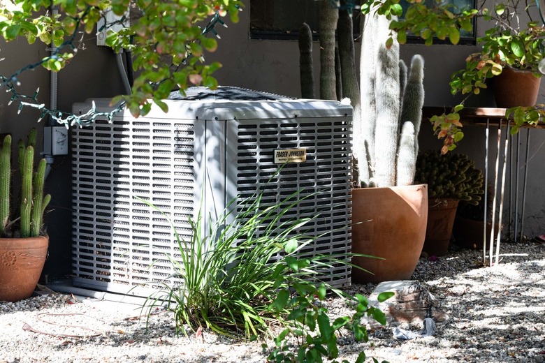 An outdoor air conditioner shaded by plants