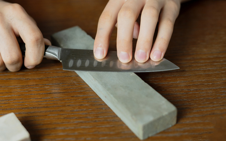 young man sharpening a knive on wooden table on dark background b