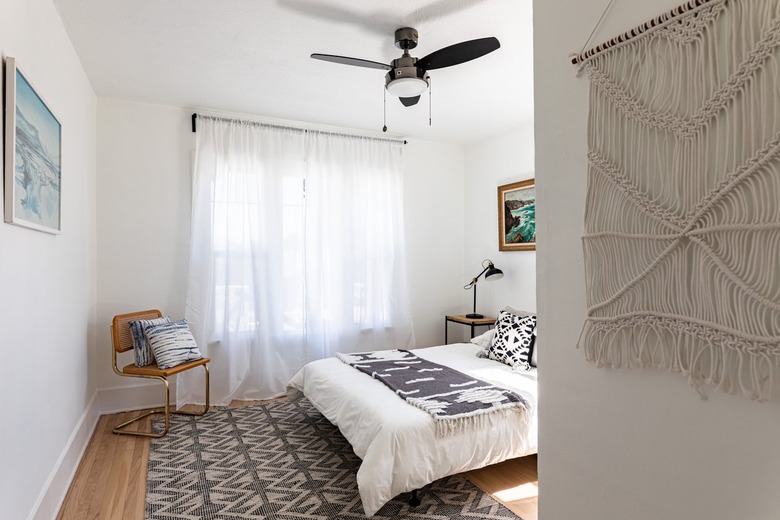 A bedroom with curtains on the window, a ceiling fan, and a macrame hanging