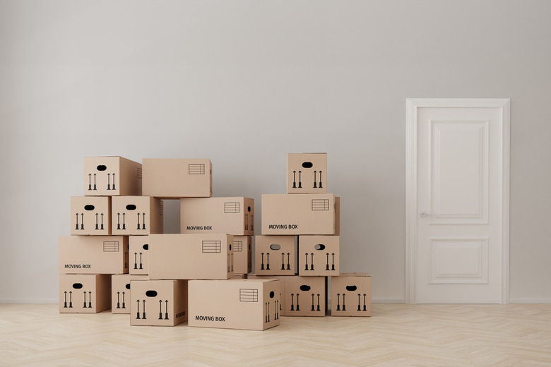 An empty apartment with cardboard moving boxes, hardwood floor, wall, door.