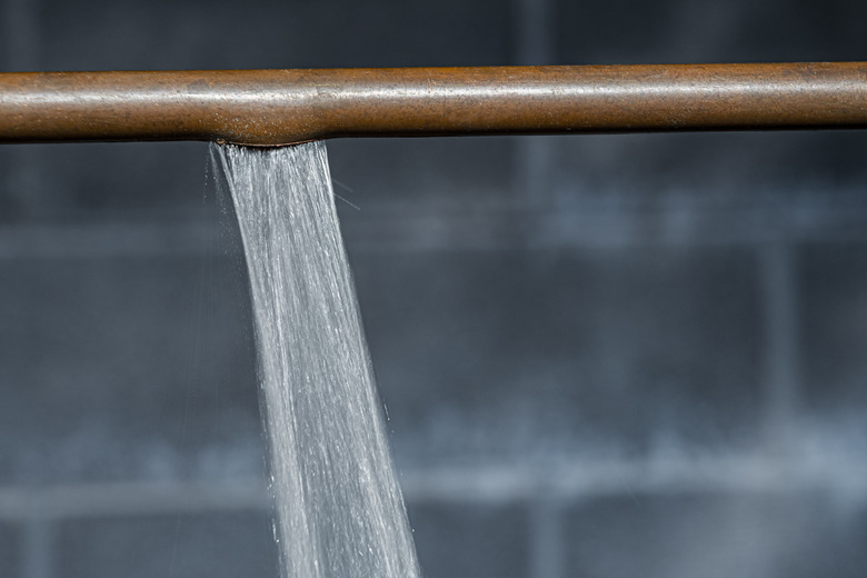 A close-up of a ruptured copper pipe spraying water against a basement wall