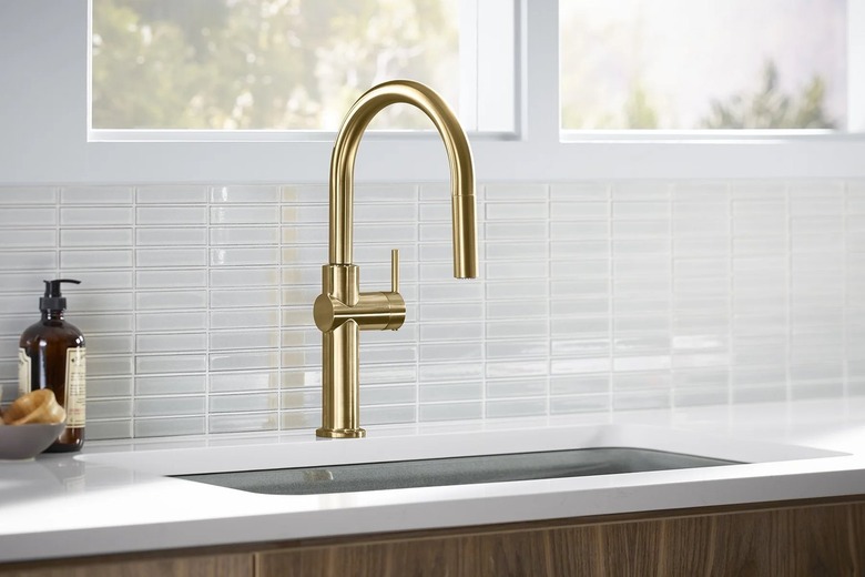 A gold faucet in a kitchen with a glass tile backsplash