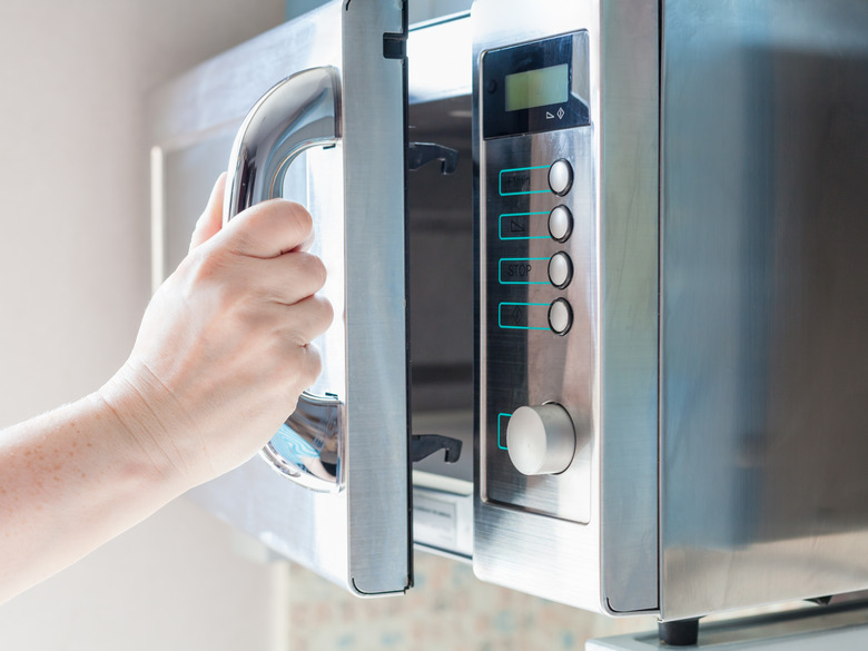 hand opens microwave oven for cooking food