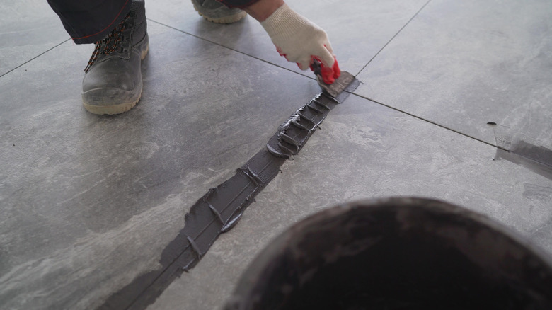 The hand of man holding a rubber float and filling joints with grout. A worker uses black grout to rub the gaps between the tiles on the floor. A worker is rubbing the tiles on the floor