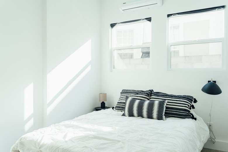 Bed with white comforter, and black and white pillows. Black sconce light fixture next to bed.