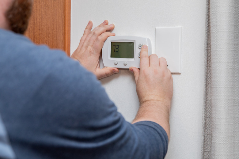 Man is pushing buttons and adjusting thermostat to change temperature at home