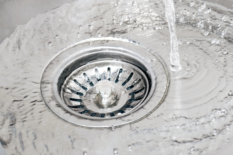 Water running from tap in a sink and pouring into drain with strainer stopper.