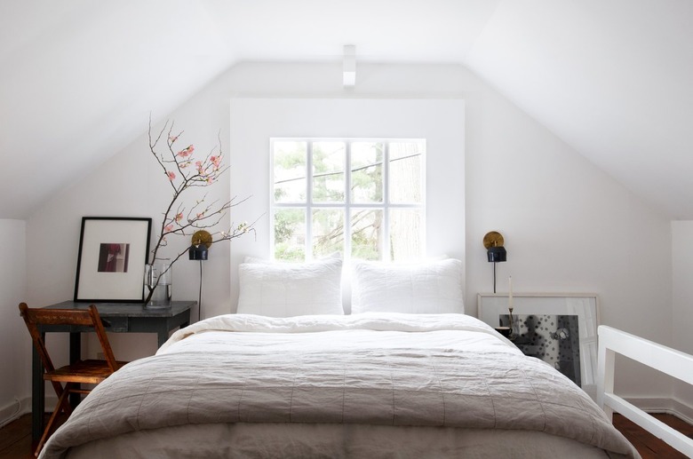 Bedroom with white walls and bedding with slanted ceiling and farmhouse furniture