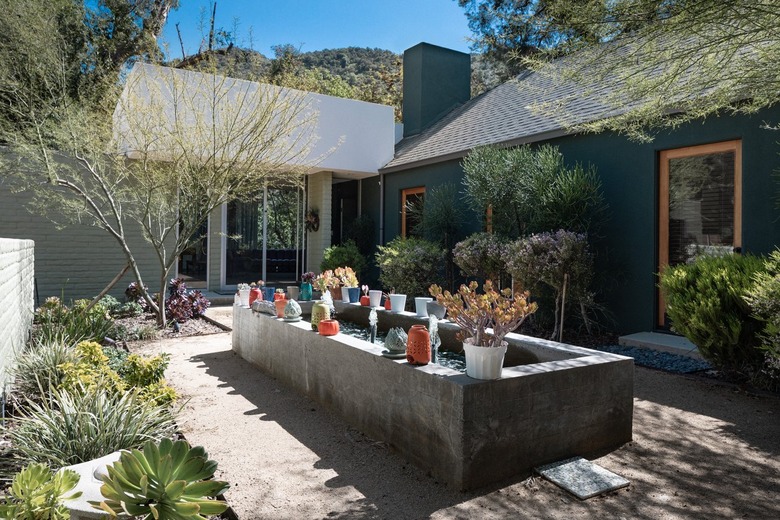 A garden box with plants in planters. Succulents and plants lining walkways, of a house.