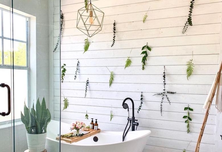 plant cutting wall in bathroom with wall white, white bathtub, glass shower, and window