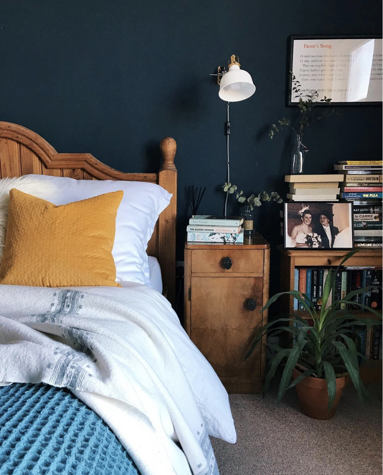 White industrial clamp light on a navy-blue wall over a wooden nightstand