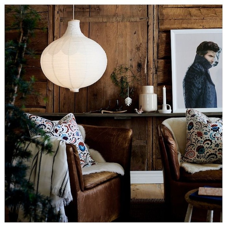 A lantern hanging from the ceiling in front of a wooden wall with a photograph and lounge chairs draped with blankets.