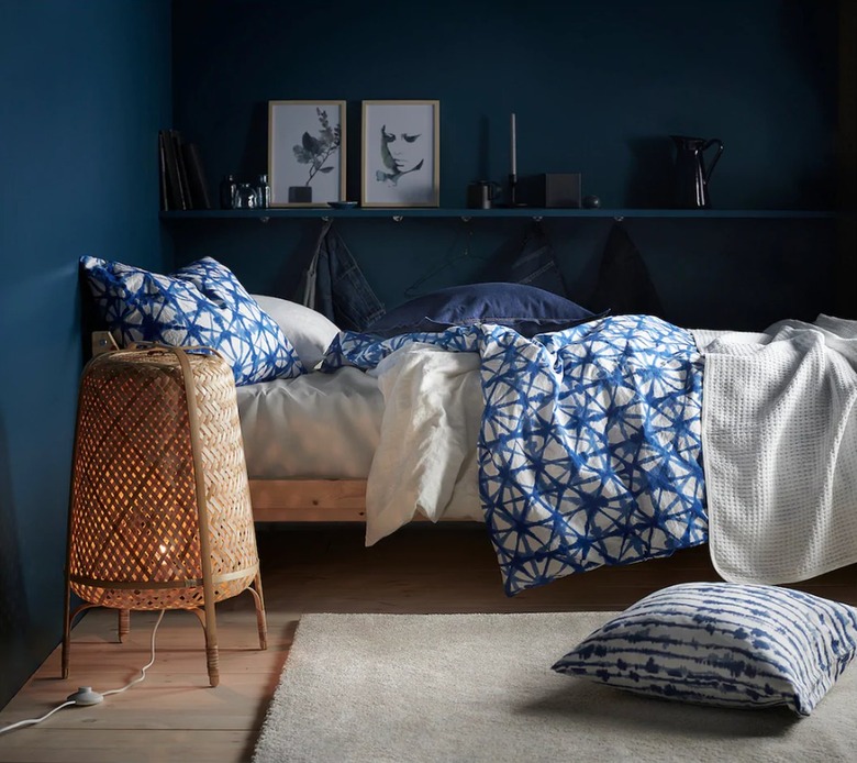 A wooden bed with blue and beige bedding in front of a navy blue wall in a darkened room.