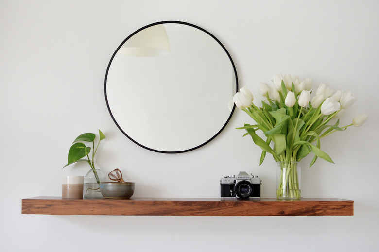 walnut floating shelf vase of white flowers, catch all bowl and wall mirror,