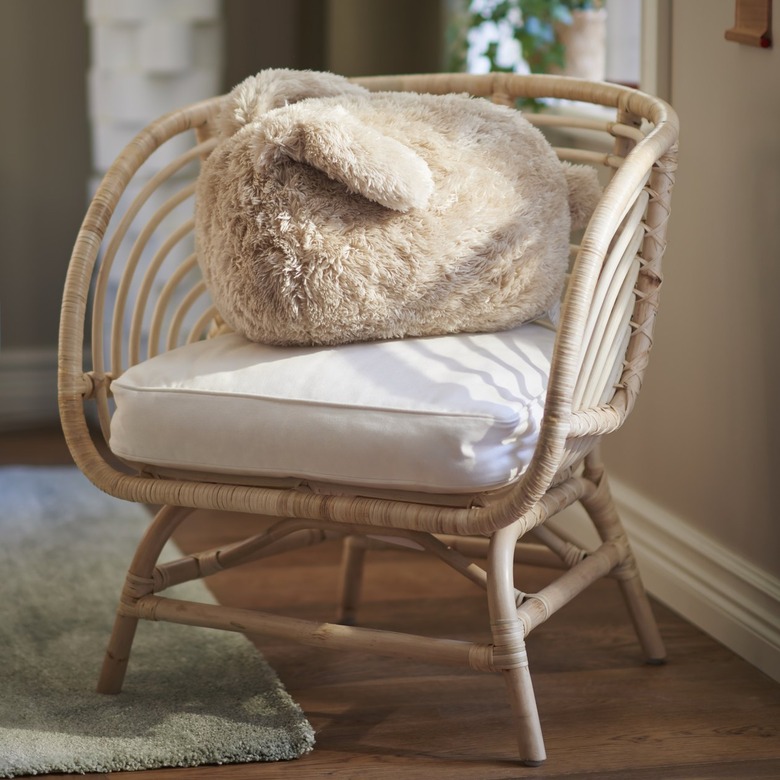 A beige bunny-shaped pillow on a woven chair with a white cushion.