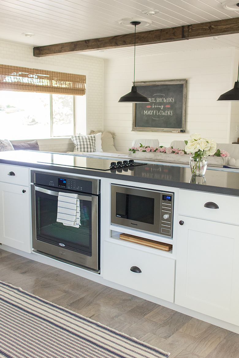 White cabinets on kitchen island with built in microwave, induction stove, black pendants lights, gray wood floor.