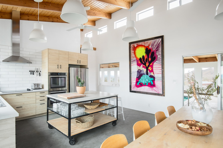 square industrial kitchen island made of metal and wood in white-tiled kitchen with stainless steel appliances