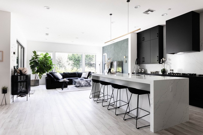 A modern kitchen with gray wood floors, black cabinets and white kitchen island