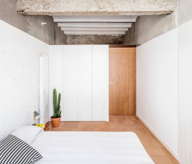 Basement bedroom with concrete ceiling, white walls, wood floor, bed.