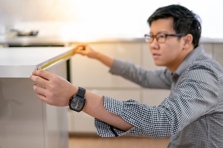 Asian man using tape measure on kitchen counter