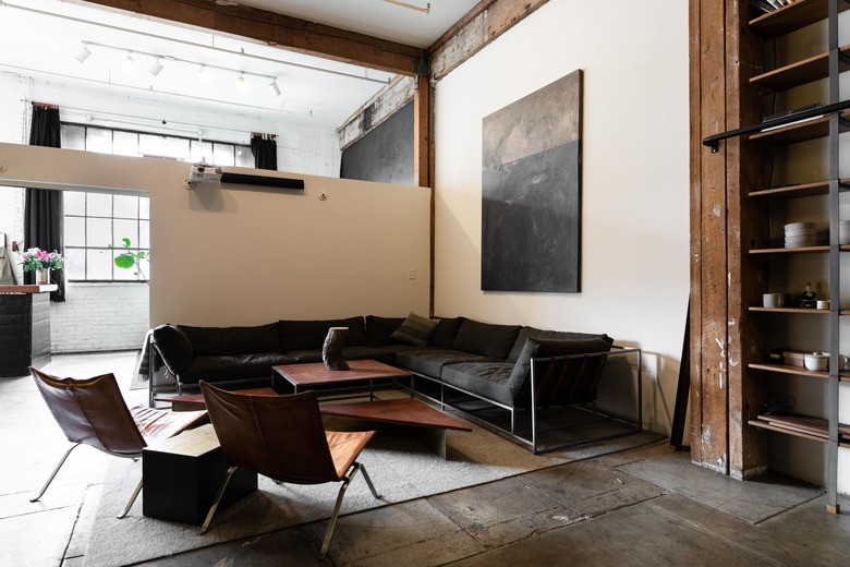 open living room with sectional, leather chairs, neutral rug, concrete floor