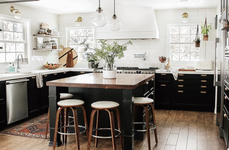 black kitchen cabinet idea for a large kitchen with white walls, lots of windows, lower black cabinets, and a black island with a wood countertop