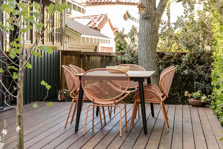 Wood deck with retro pink chairs, surrounding a picnic table, with surrounding trees.