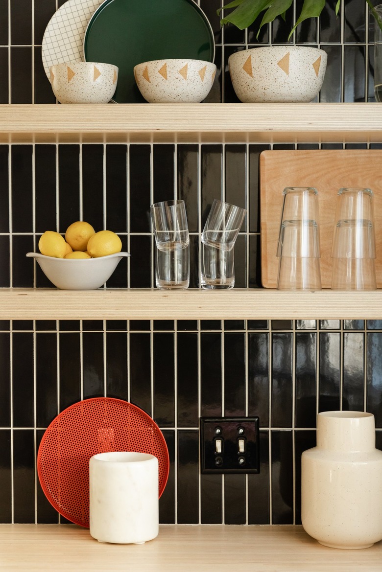 Wood kitchen shelves with dishware and black rectangular tile backsplash