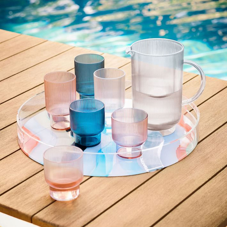 Blue, pink, and clear acrylic drinkware on round tray by the pool