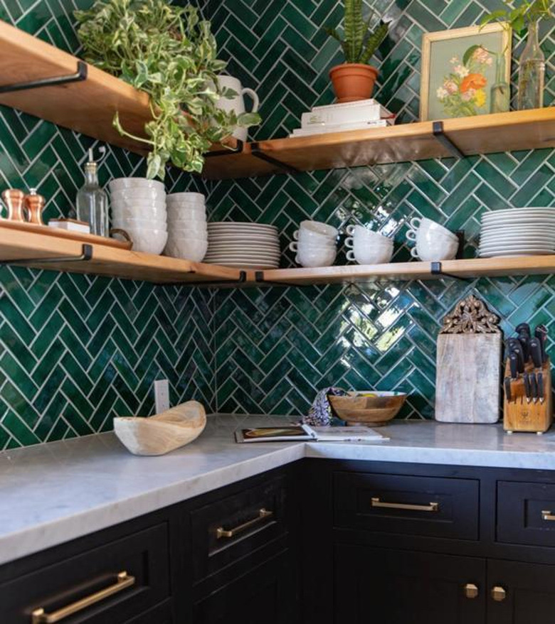 herringbone green tile kitchen backsplash with wood open shelving and black cabinets