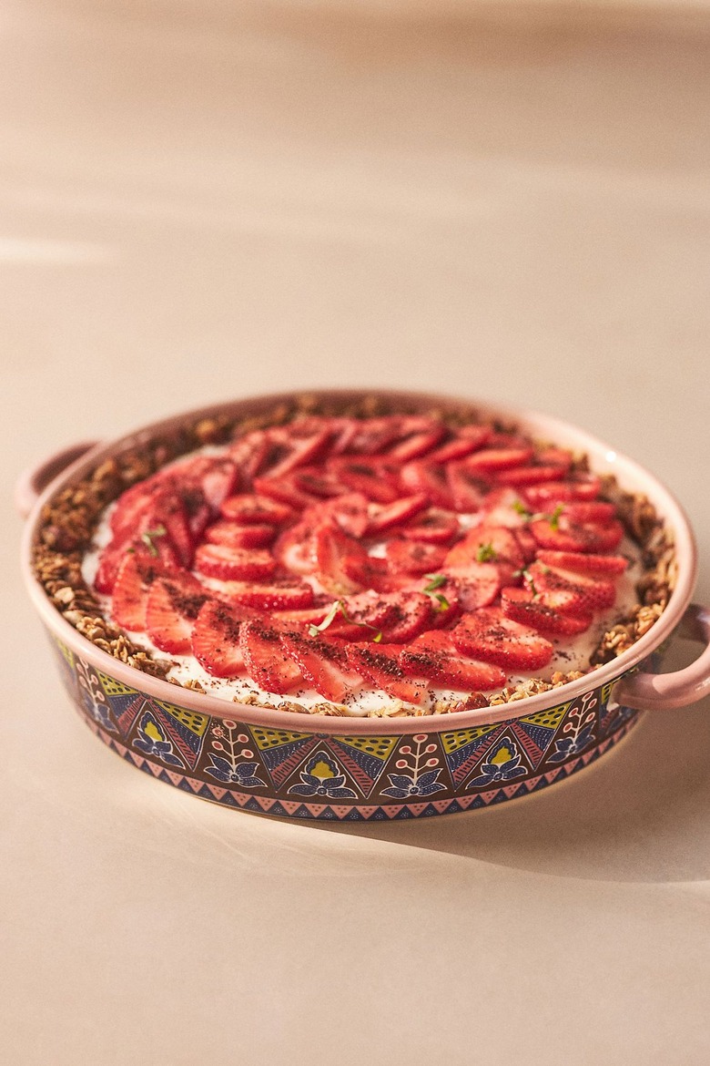 A strawberry tart rests on a counter in an ornately designed pie platter, that features a dark blue, purple and green floral pattern.