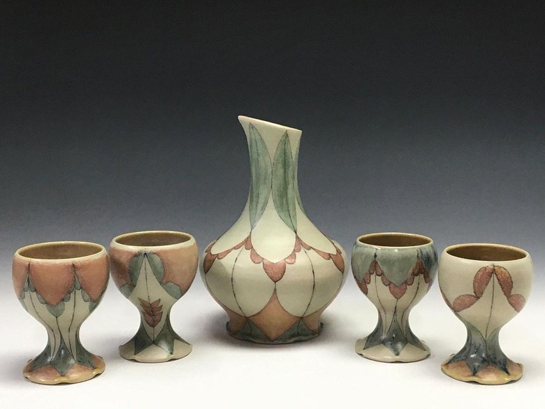 Four wine-glass shaped ceramic cups surrounding a patterned vase.