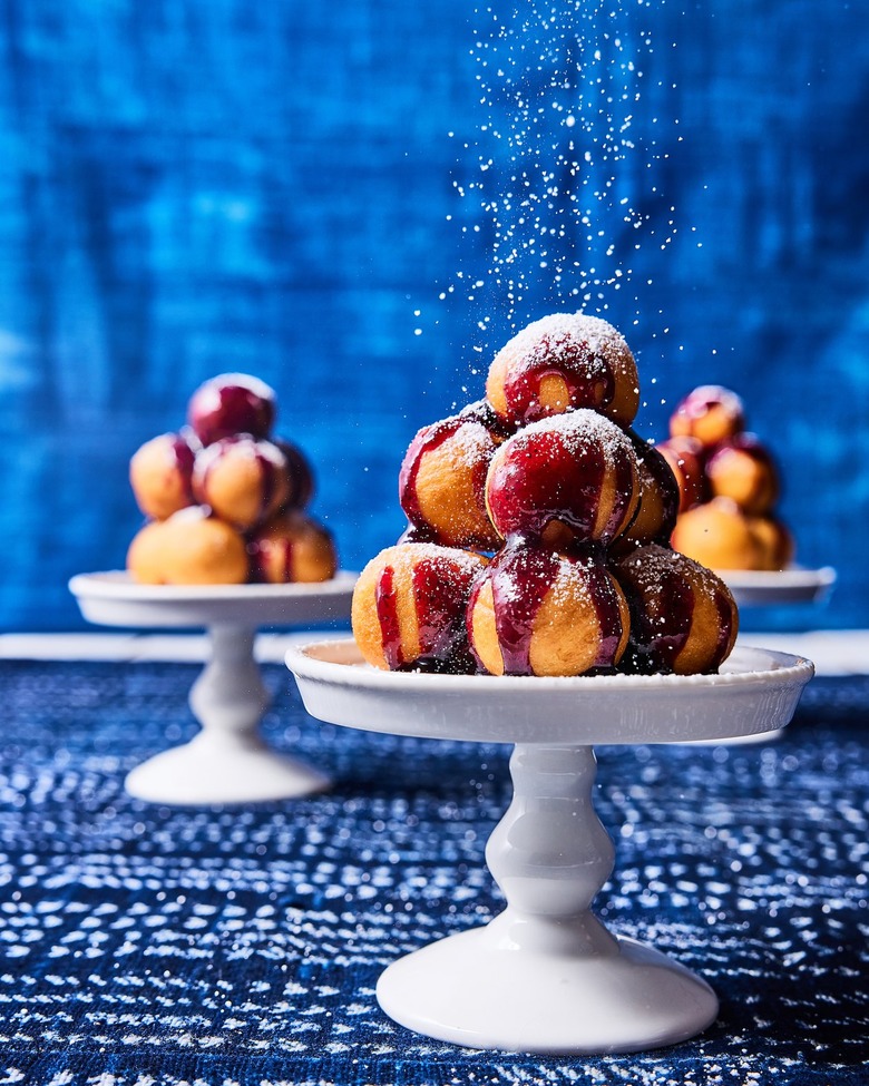 A white serving tray piled high with croquembouche on a blue tablecloth in front of a blue curtain.