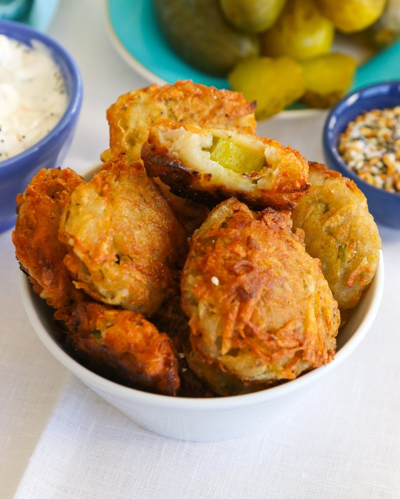 A white bowl of fried pickle latkes with a bite taken out of one of them.