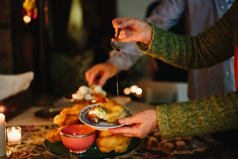 Hands holding a plate of Moroccan donuts and drizzling it with honey.