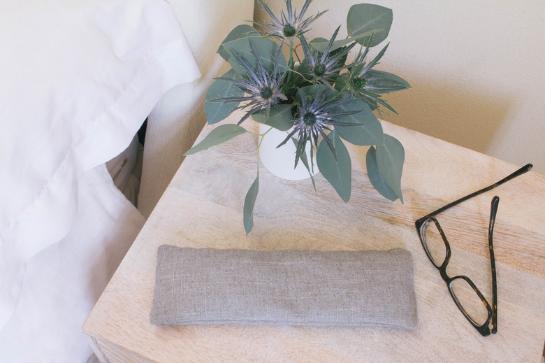 Eye pillow sitting on night stand with glasses and flowers