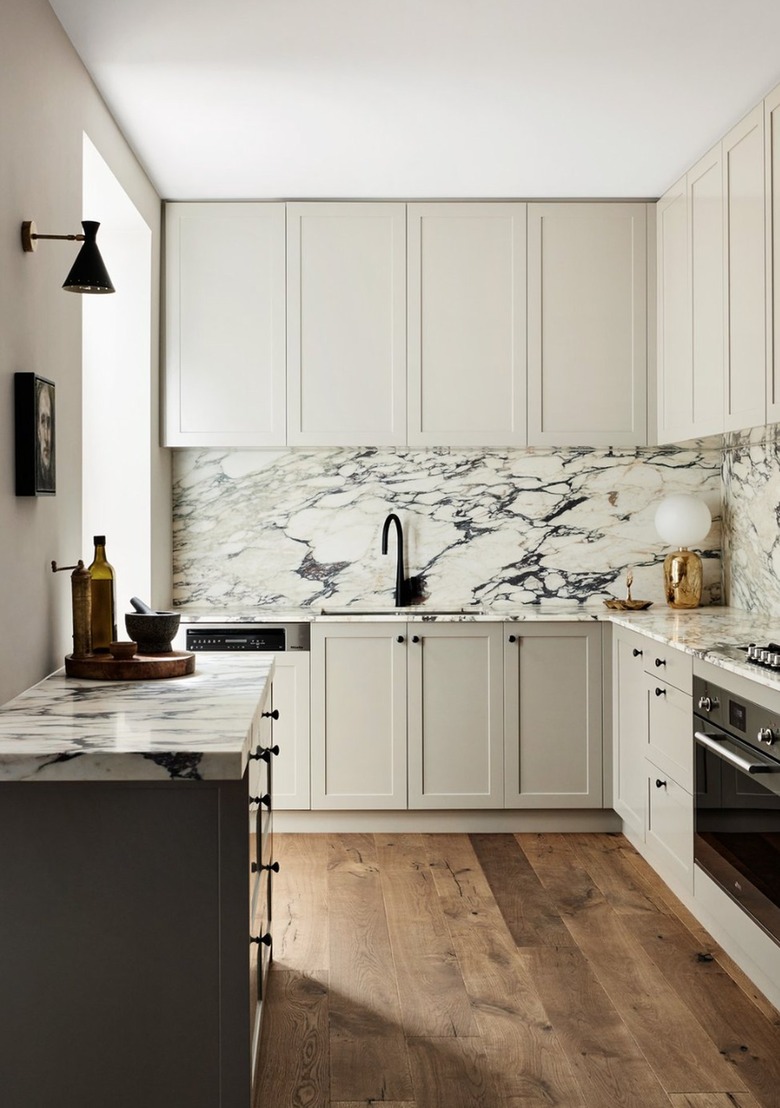 Kitchen with greige cabinets, black appliances and black and white marble counters and backsplash.