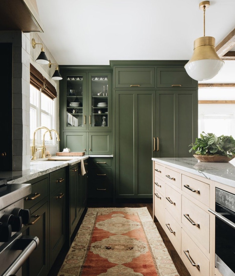 Kitchen with dark green cabinets, beige island and gold hardware.